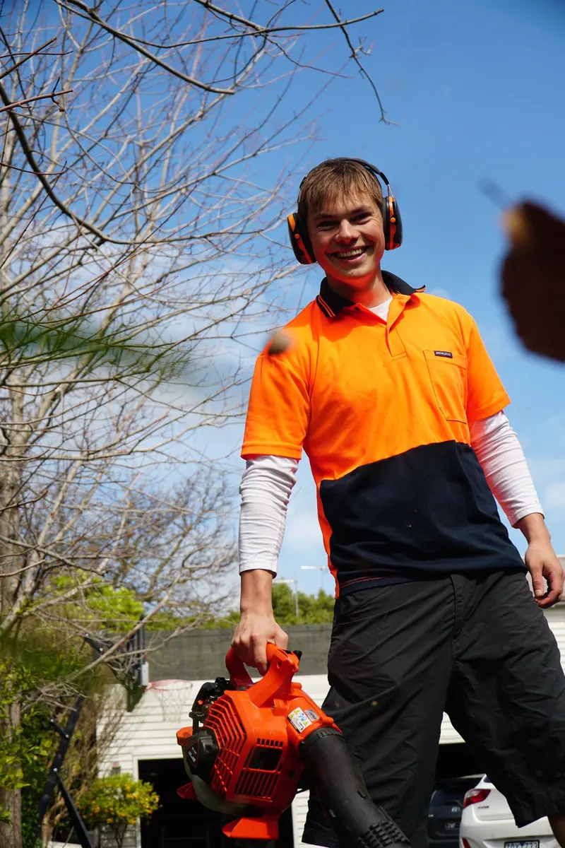 Henry of HP Gardening smiling, holding a blower under a blue sky