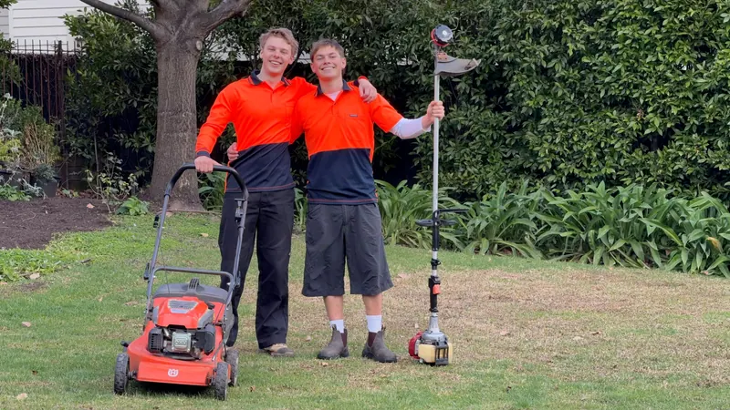Hamish and Henry of HP Gardening standing together on a lawn with their mower and line trimmer