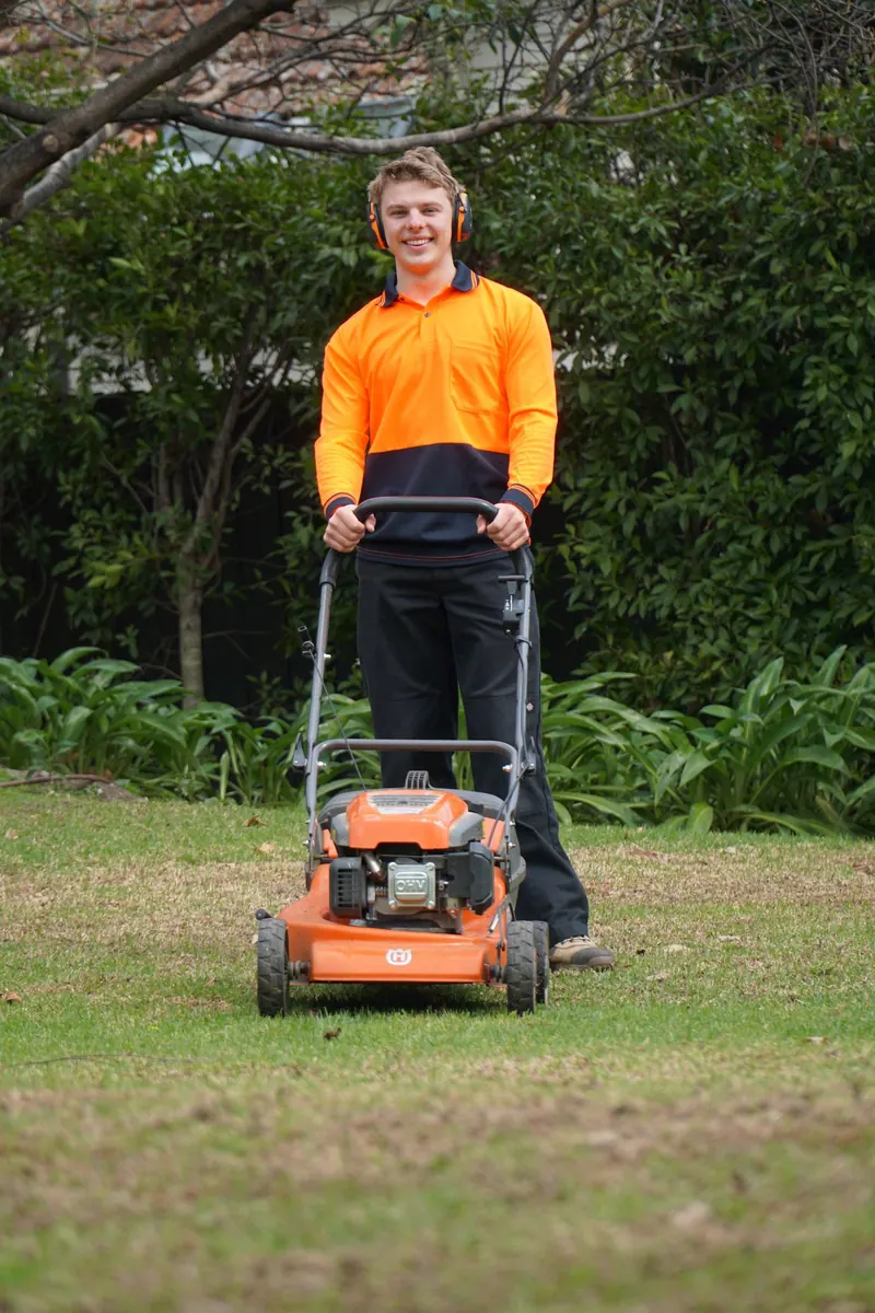 Hamish pushing a mower across a back lawn
